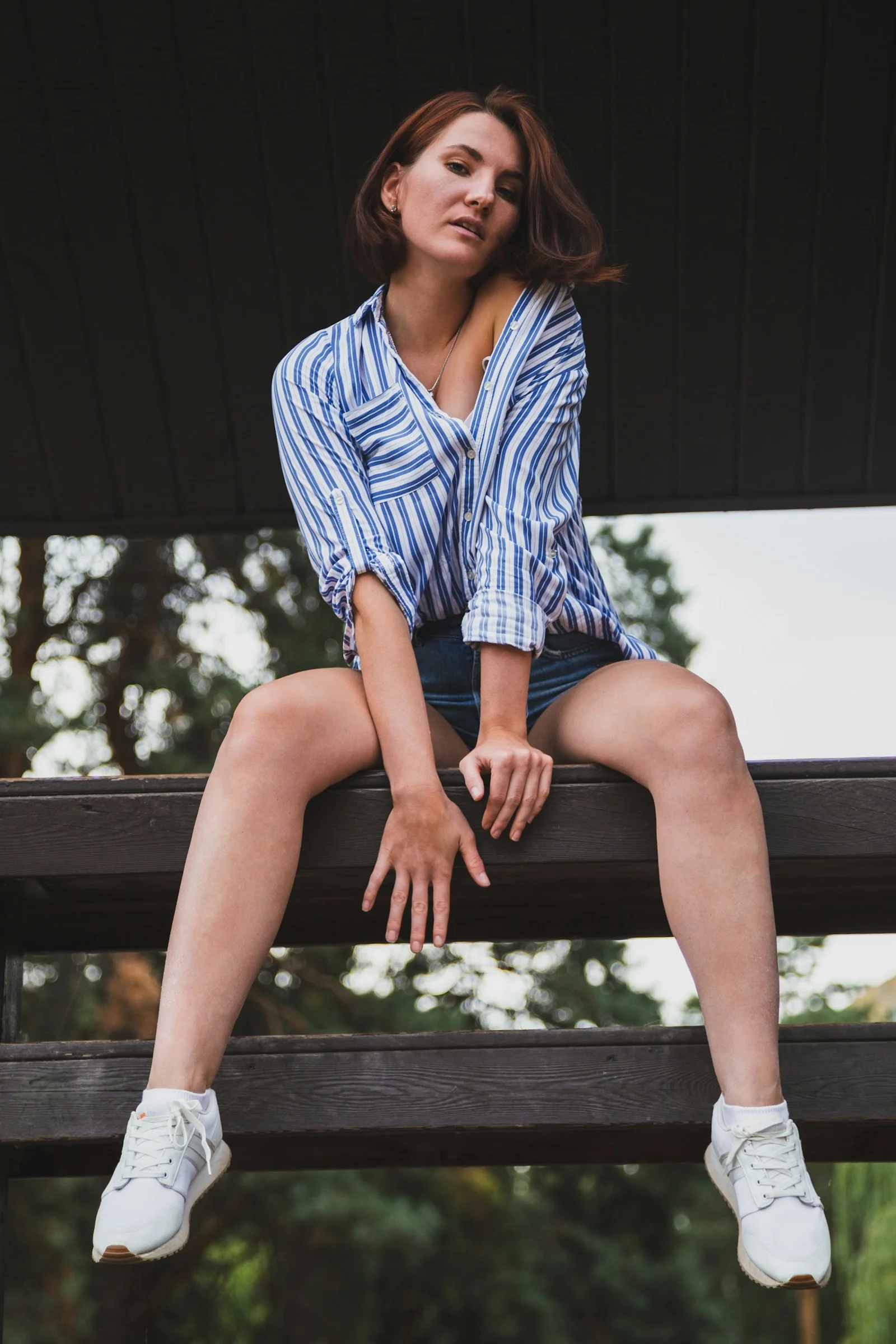 身穿蓝白条纹衬衫坐在黑色木制长椅上的女子