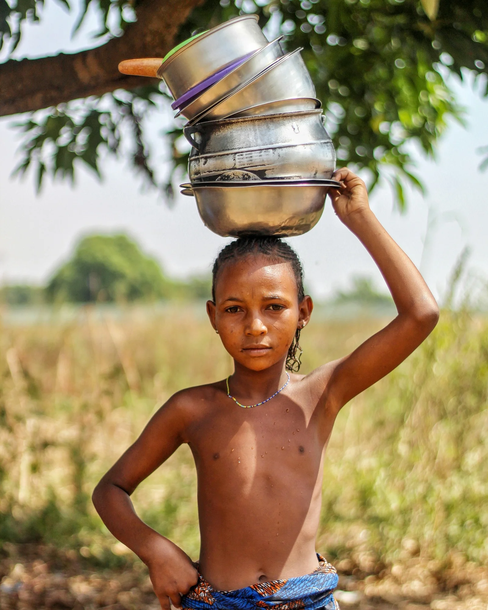 a young girl carrying a pot on her head