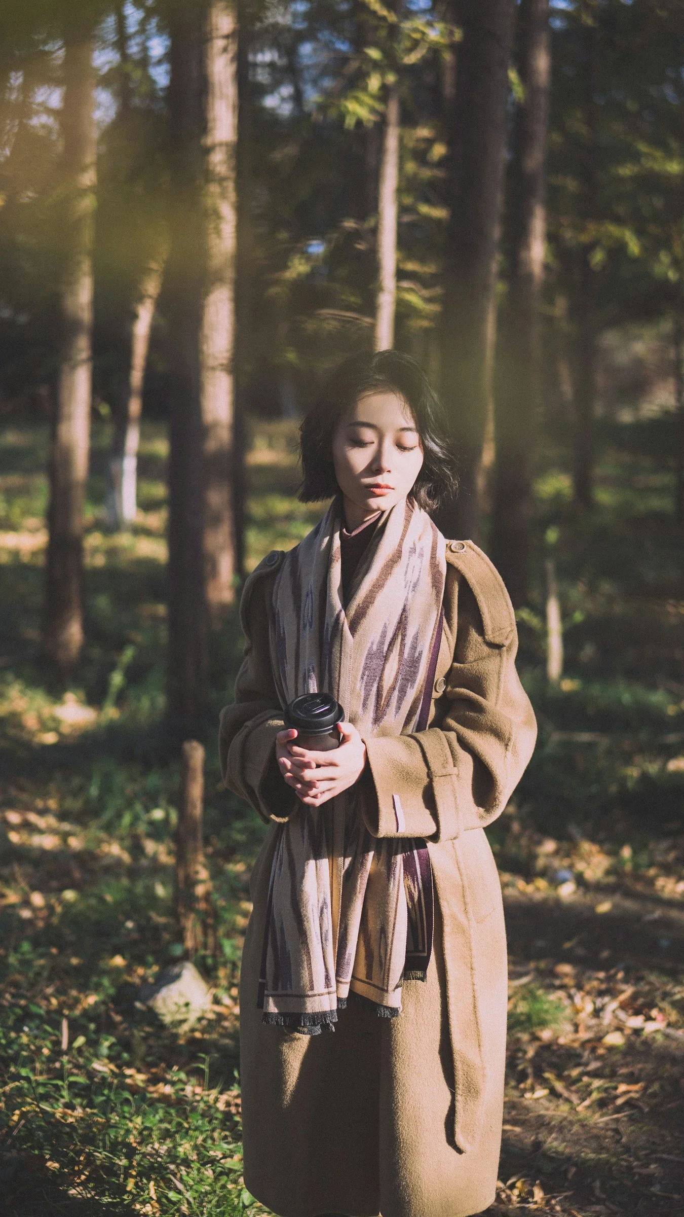 A woman standing in the woods wearing a long coat