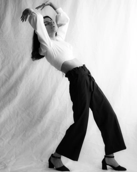 woman in white long sleeve shirt and black pants lying on white textile