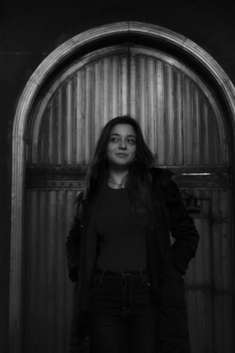 A black and white photo of a woman standing in front of a door