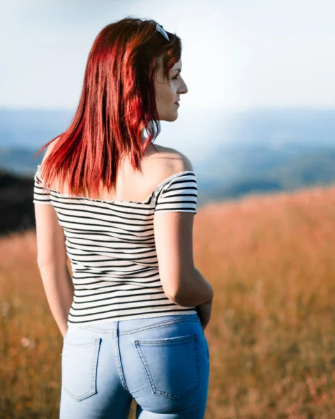 woman in white and black stripe shirt and blue denim jeans standing on brown grass field
