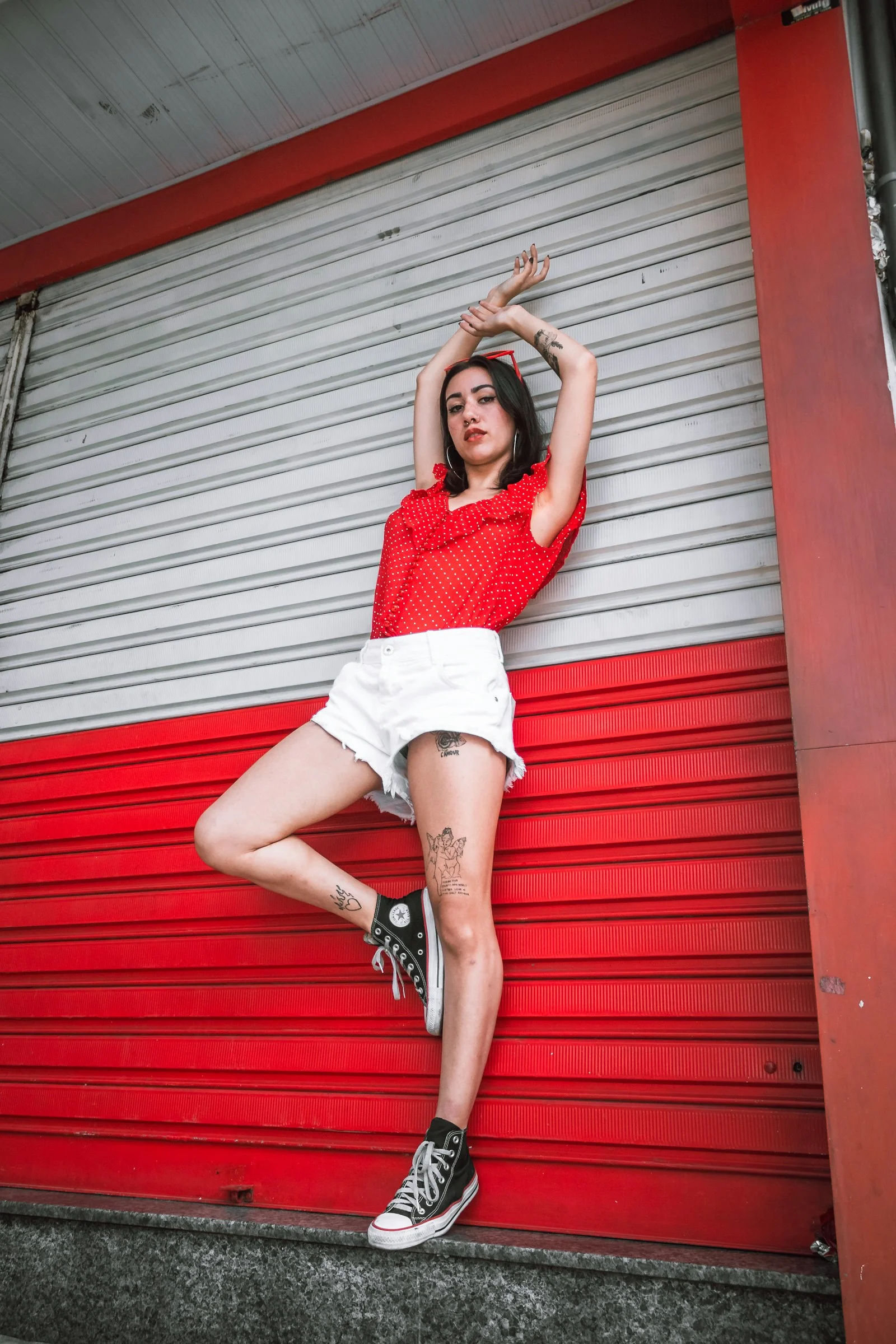 woman wearing red sleeveless shirt and white short shorts leaning on white-and-red roll-up door