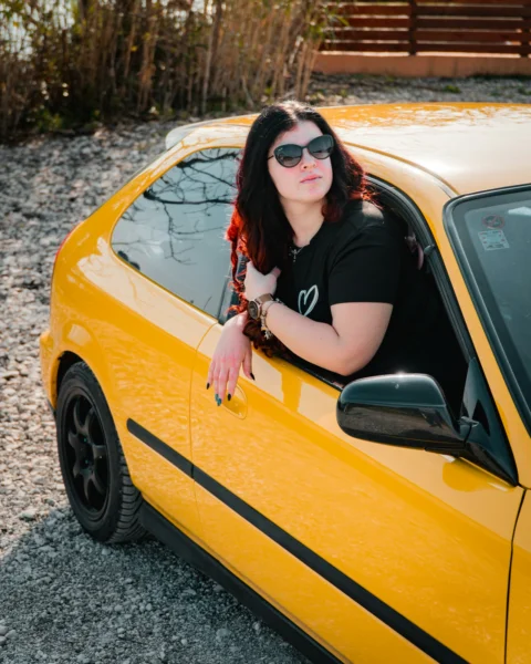 A woman poses in a yellow car