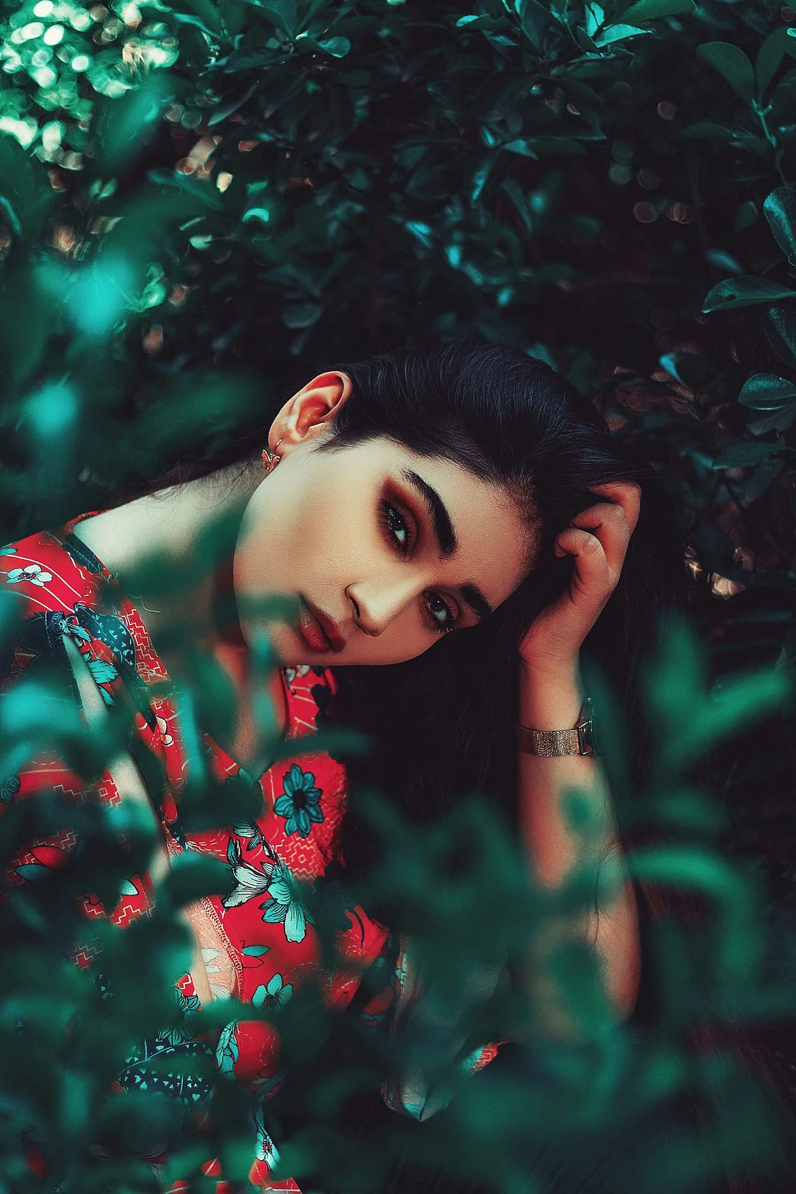 A woman in a red floral top framed by dark green foliage