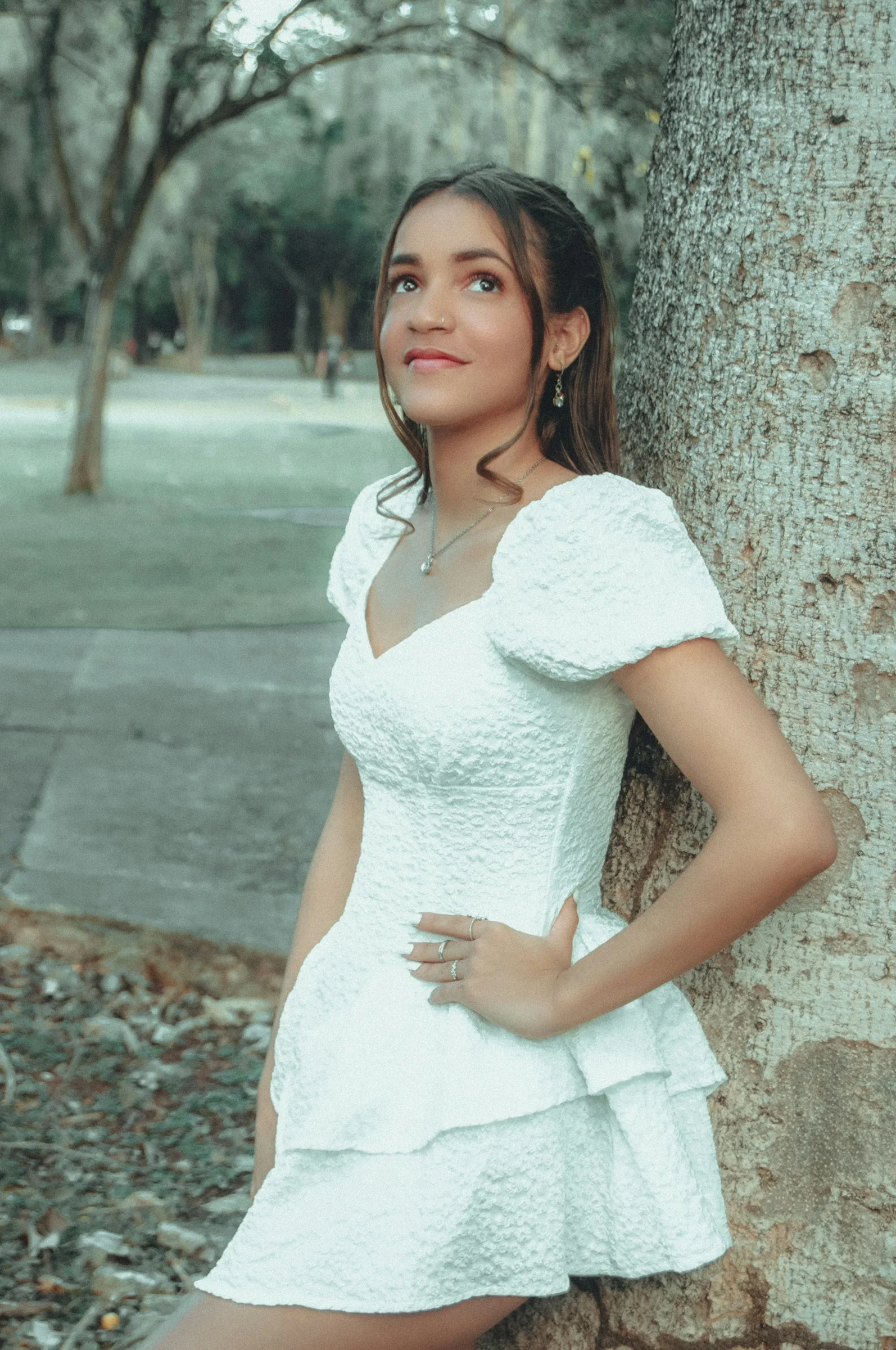 a woman in a white dress leaning against a tree