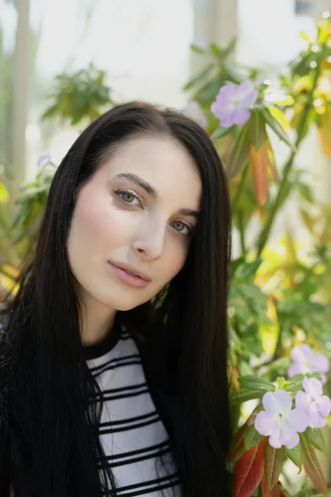 Young woman with dark hair stands near purple flowers