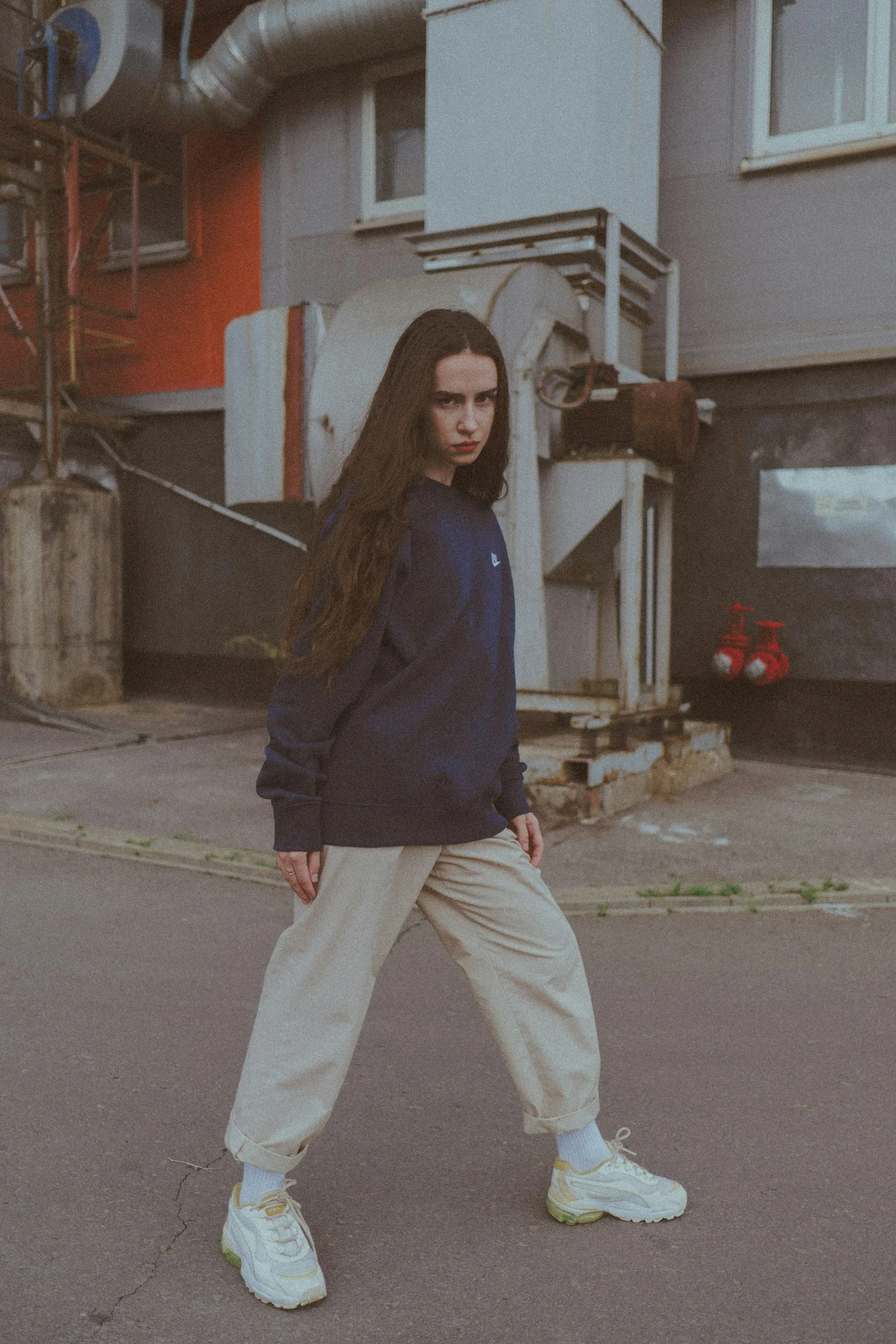 woman in brown sweater and white pants standing on gray asphalt road during daytime