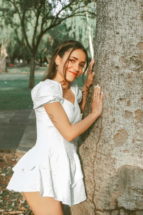 a woman in a white dress leaning against a tree