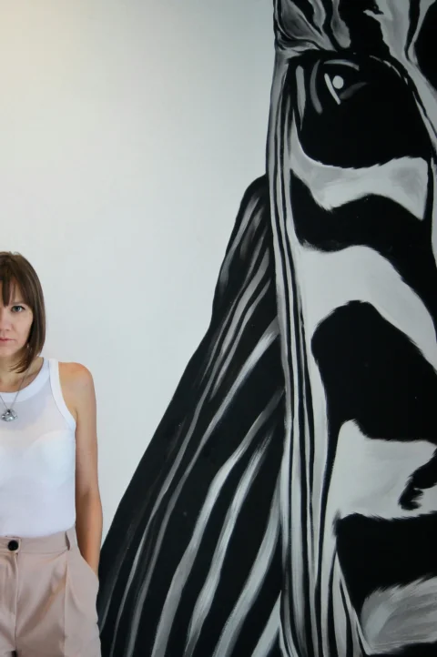 a woman standing in front of a painting of a zebra