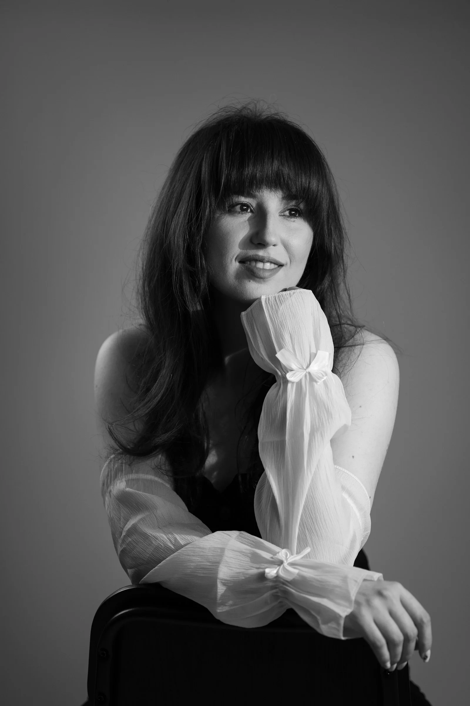 Young woman with bangs smiles, resting chin on hand