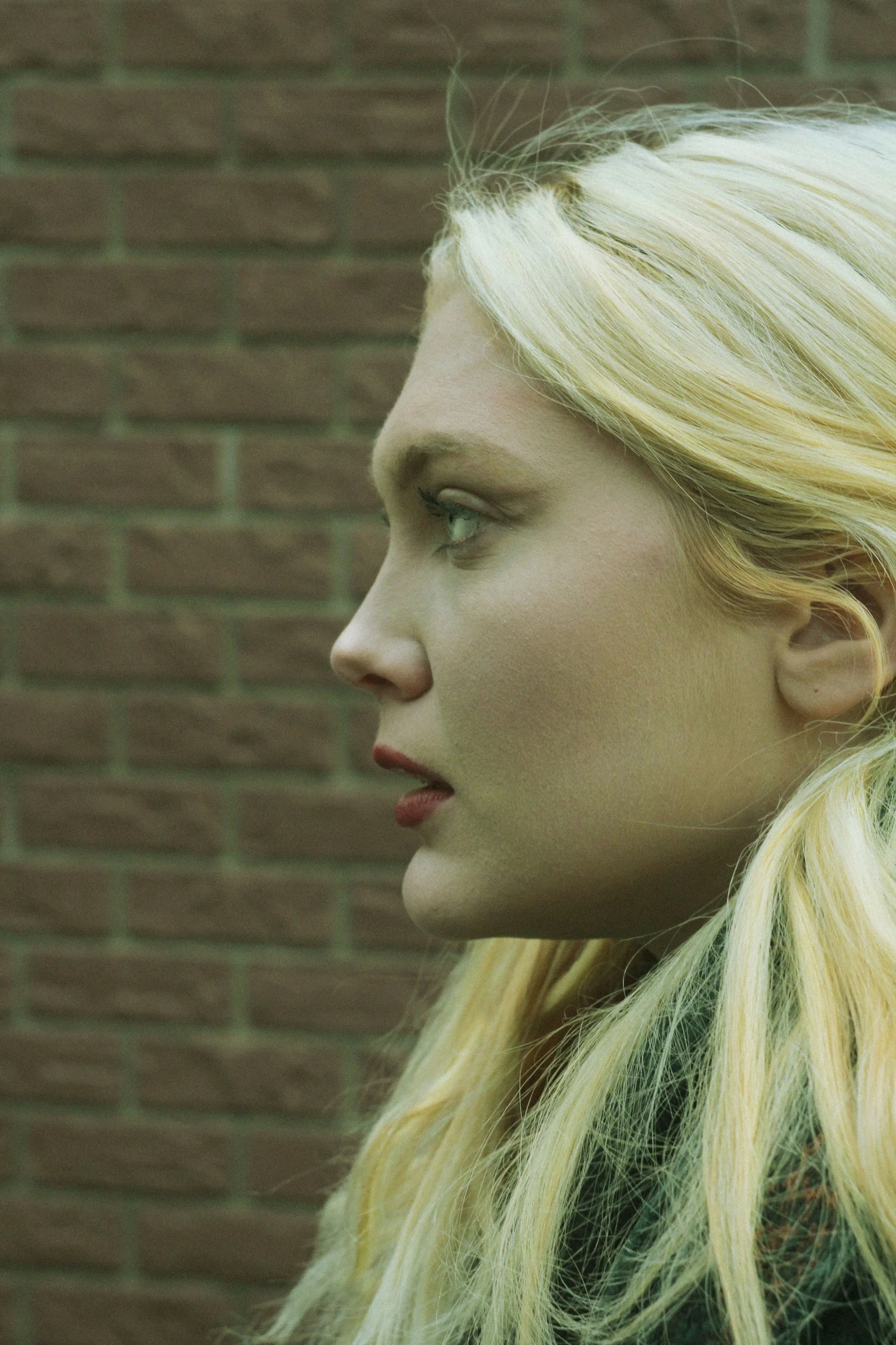 A woman with long blonde hair standing in front of a brick wall