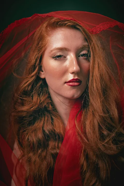 Woman with long red hair veiled in red fabric