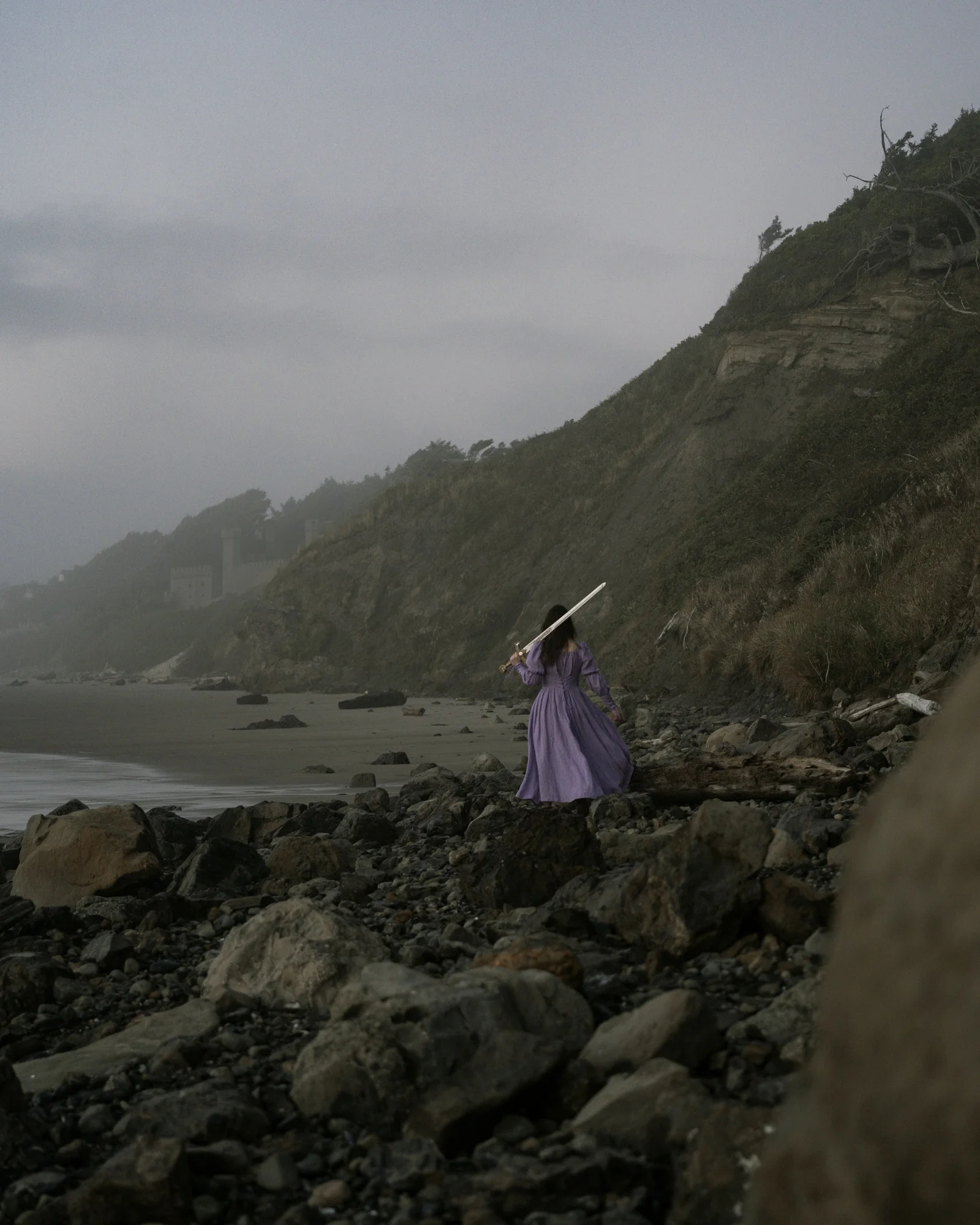 a woman in a purple dress is walking on a rocky beach