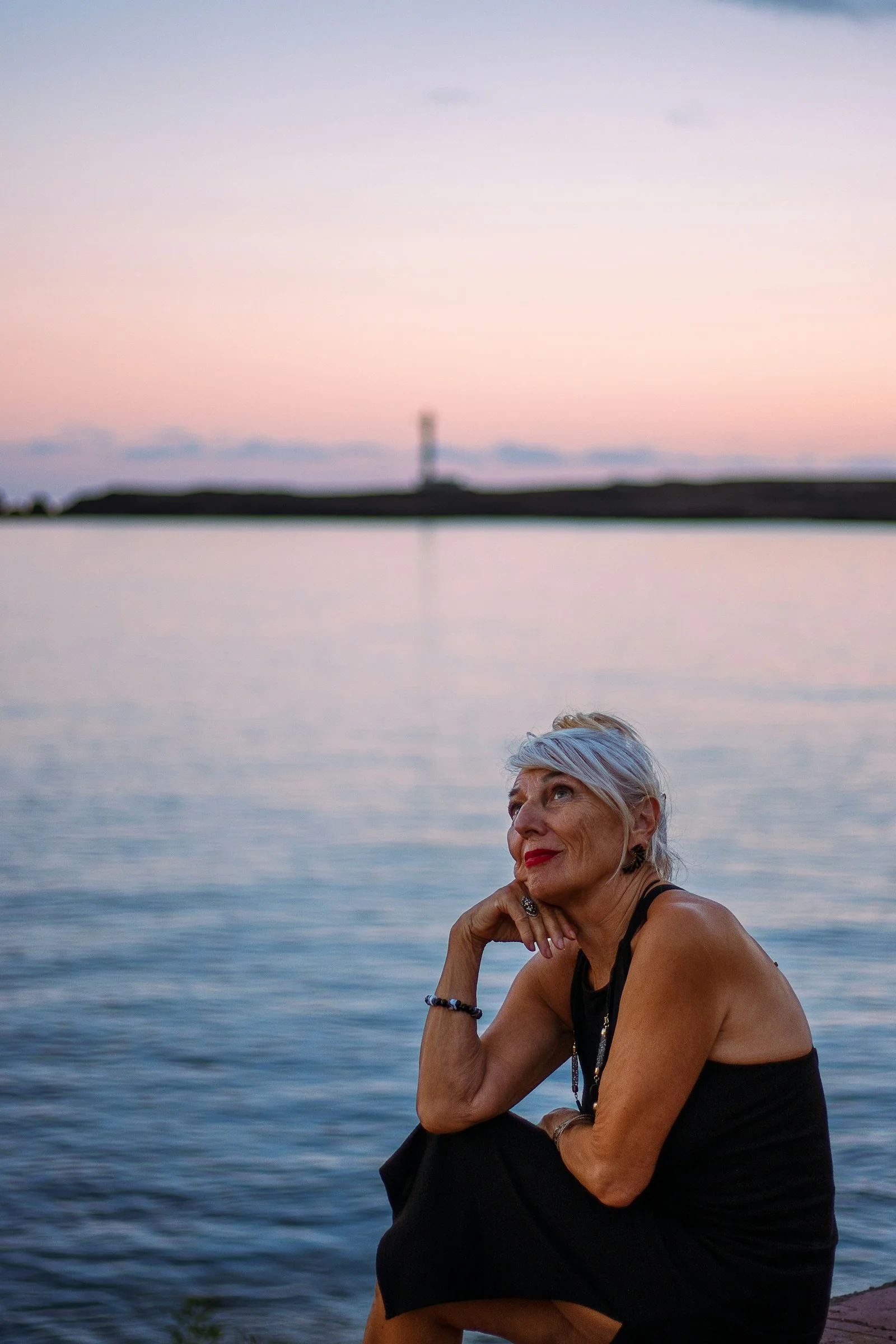 Woman looking up at a pastel sunset over water