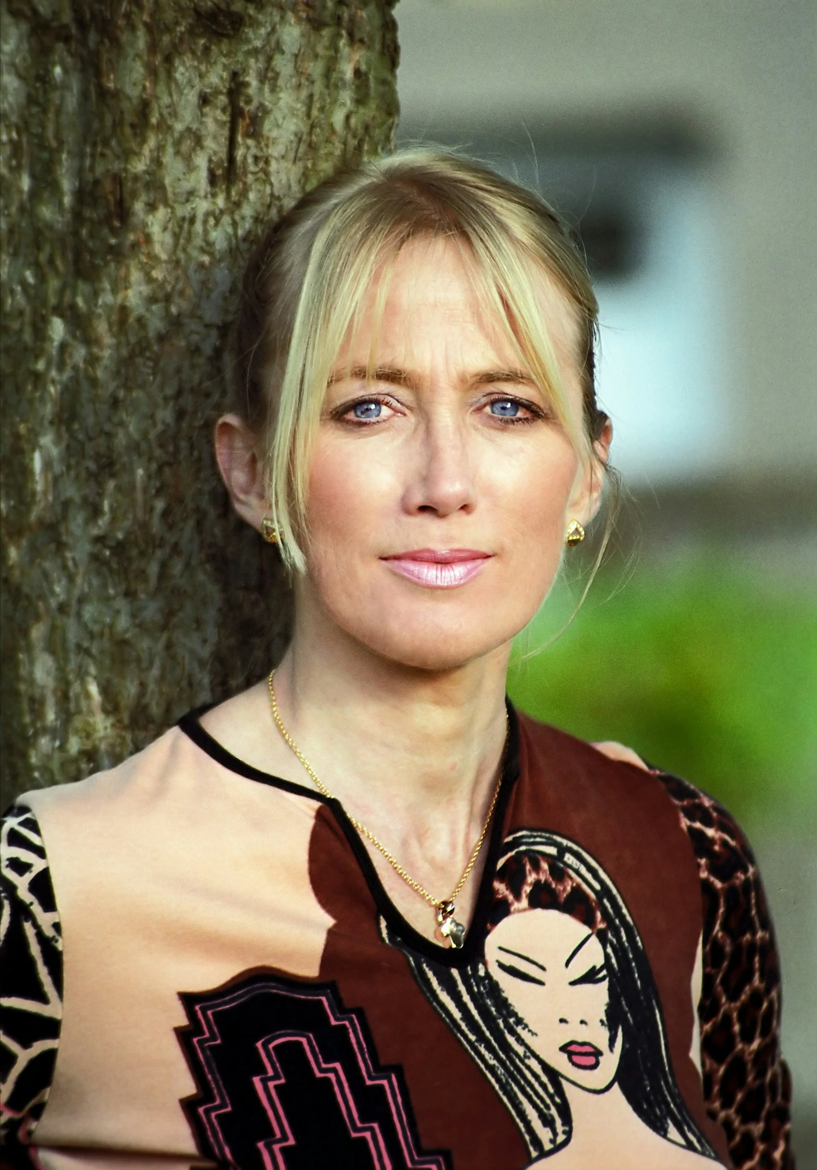Blonde woman with blue eyes leaning against tree