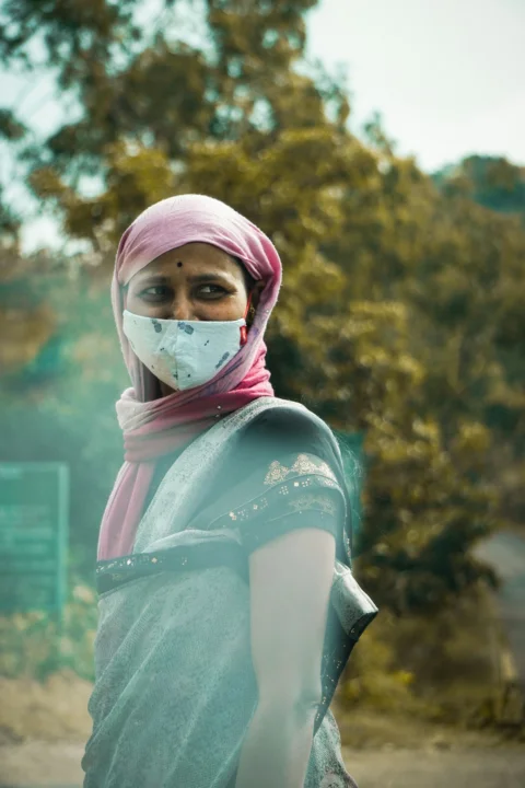 a woman wearing a face mask standing in front of a tree