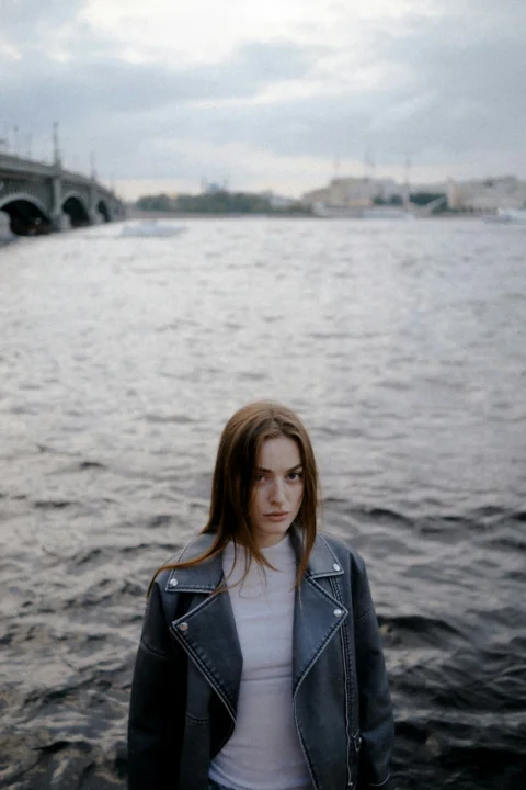 Young woman stands by a river with bridge