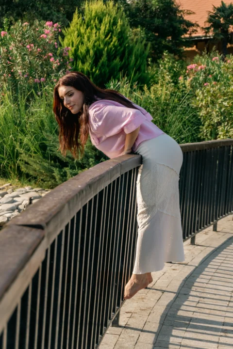 A woman in a pink shirt and white skirt leaning over a metal railing