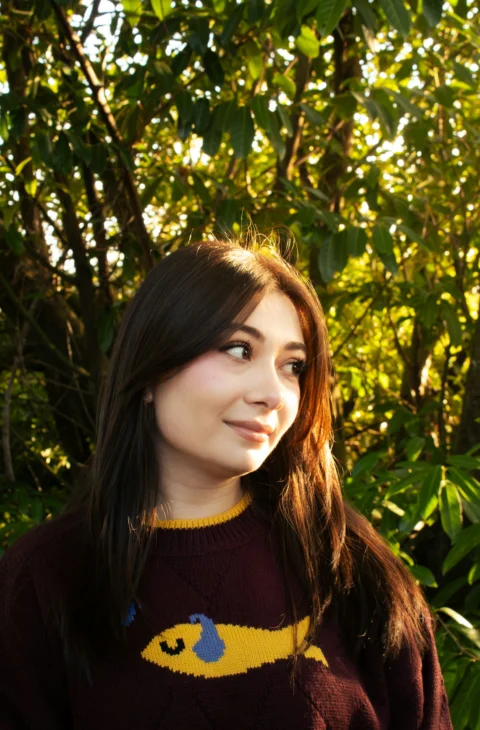 Young woman with dark hair wearing a sweater outdoors