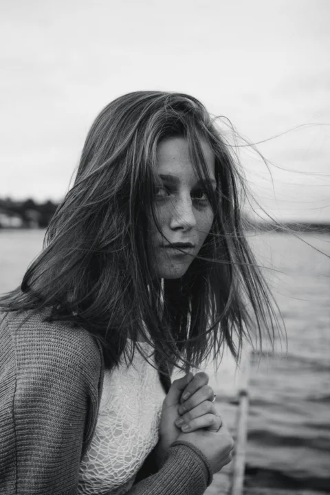 A woman with long hair standing next to a body of water