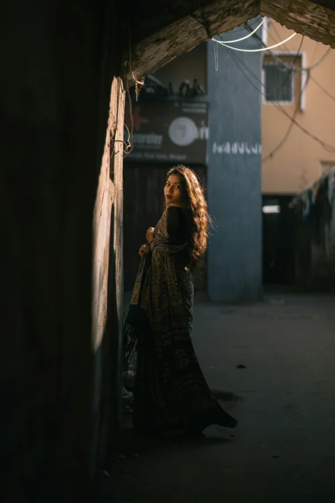 Woman in a sari standing in a sunlit alleyway