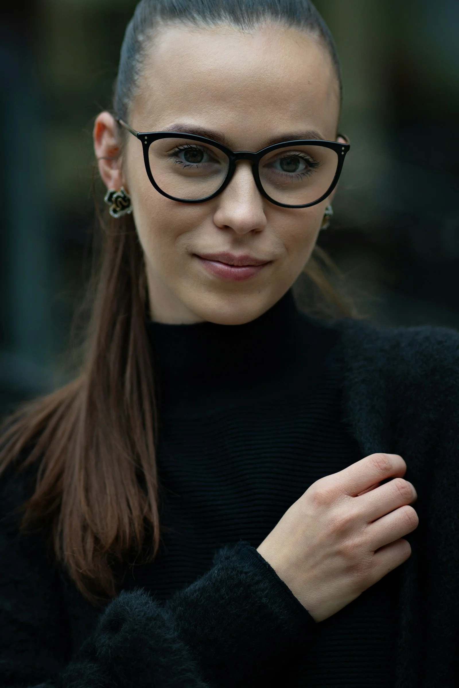 A woman with long brown hair wearing black glasses and a black sweater