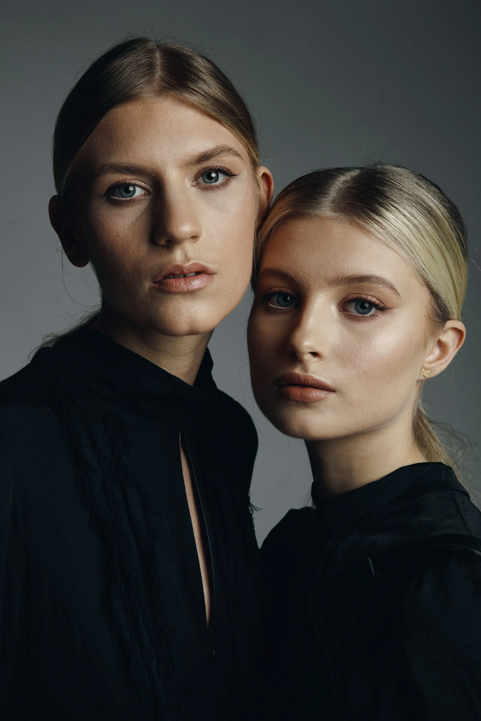 Two blonde women in black tops against a grey background