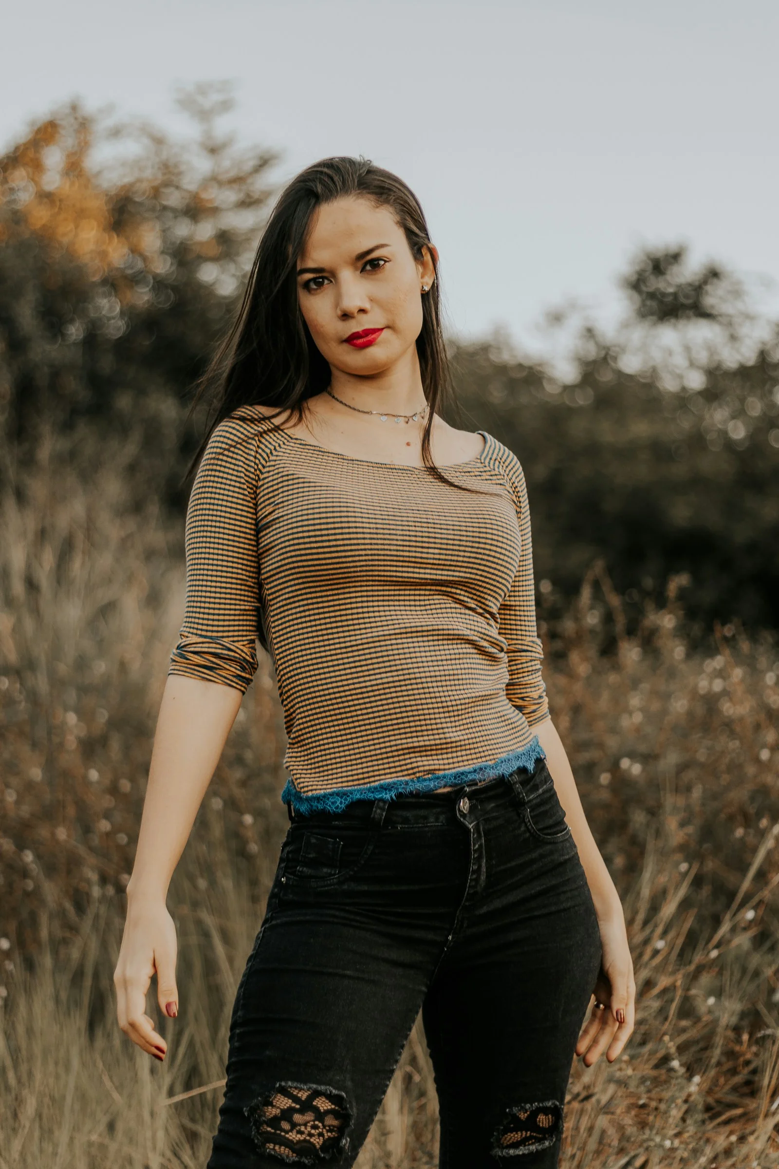 woman in brown long sleeve shirt and black denim jeans standing on grass field during daytime