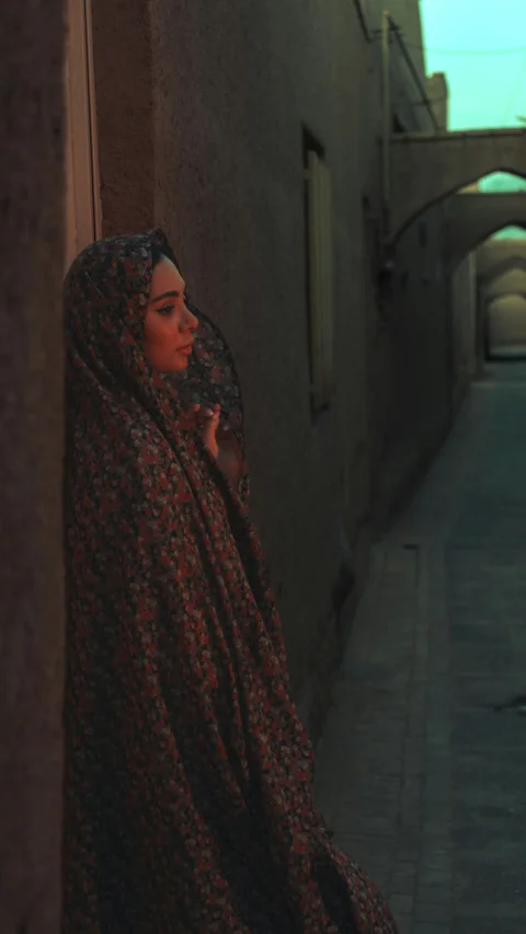 A woman in a hijab stands in a dim alley