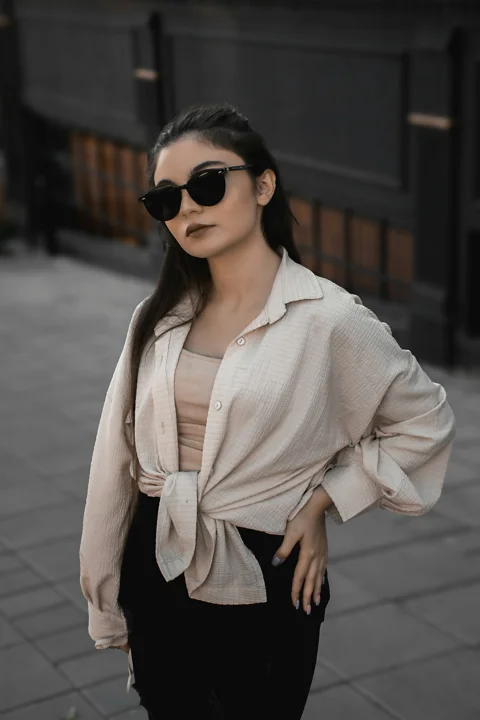 A woman standing on a sidewalk wearing sunglasses