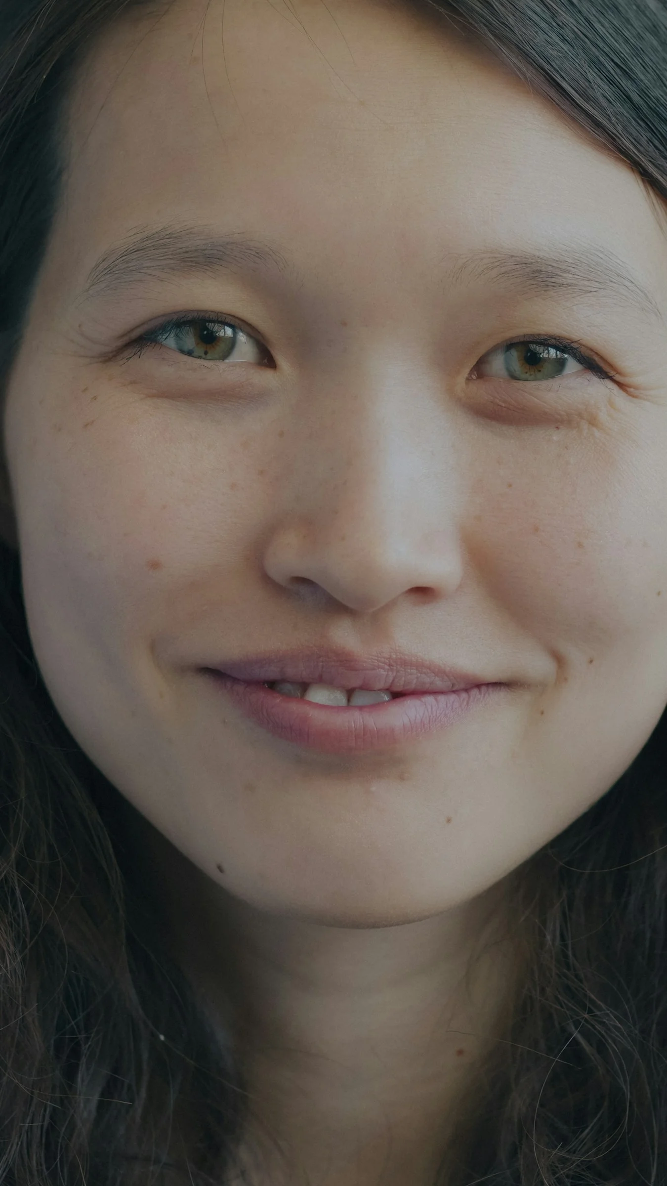 A close-up portrait of a smiling woman with freckles and light green eyes