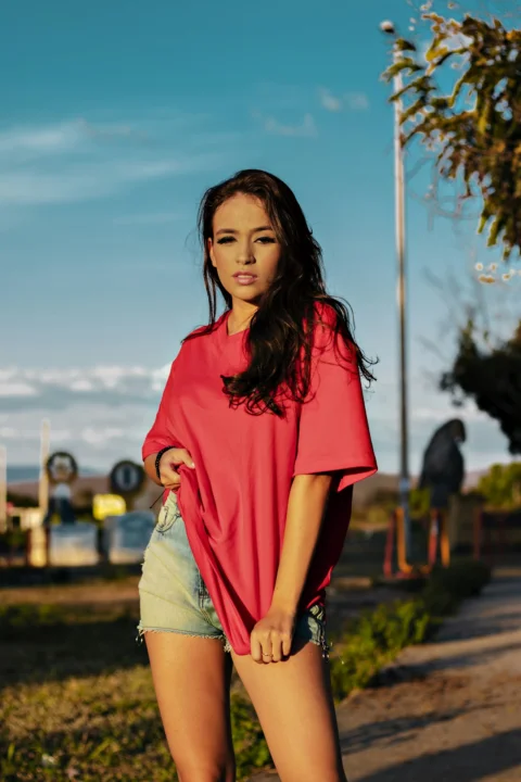 白天,一位身穿红色 Polo 衫和棕色牛仔短裤的女士站在绿色草地旁