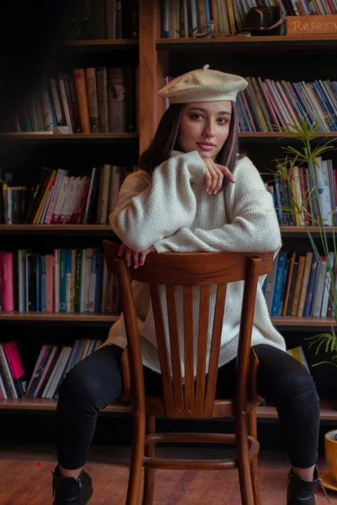 Young woman wearing a beret and sweater sits on chair