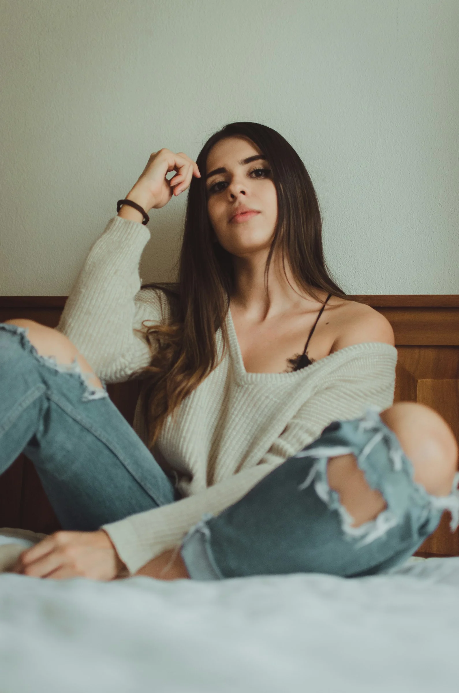グレーのVネックセーターを着た女性がベッドに座っている