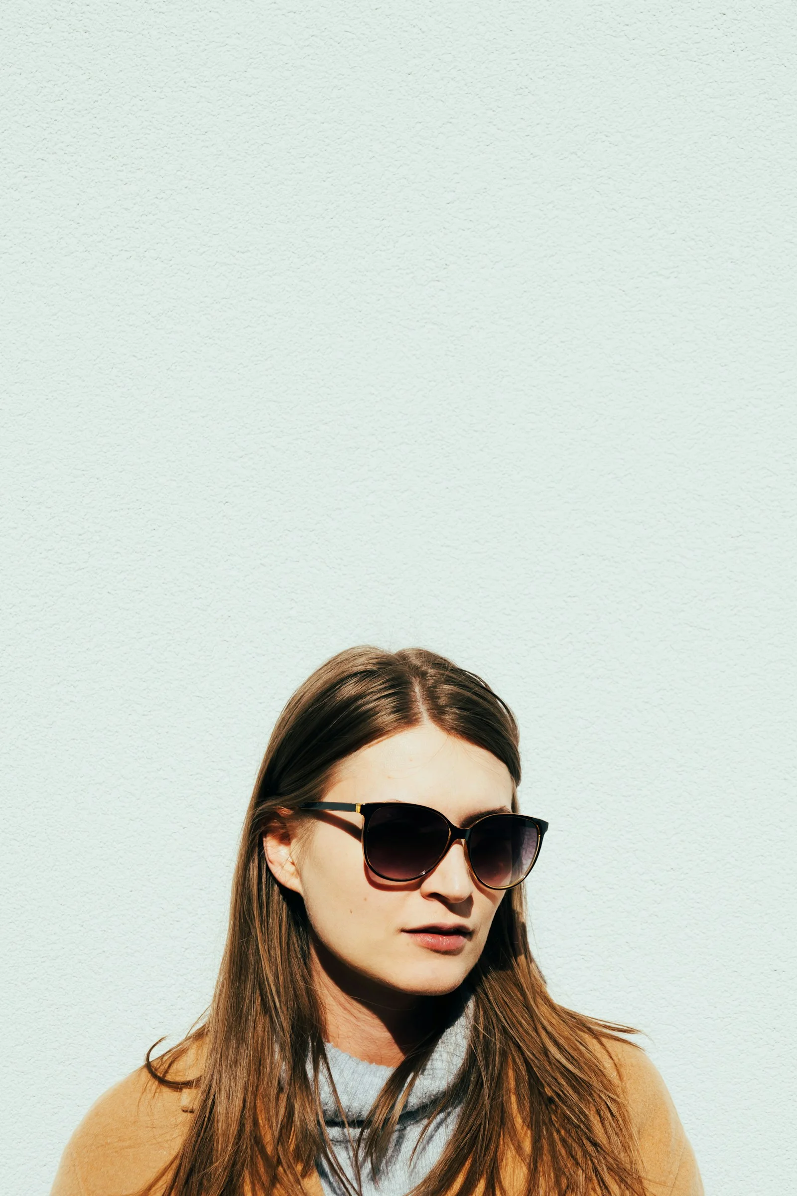 a woman wearing sunglasses standing in front of a white wall