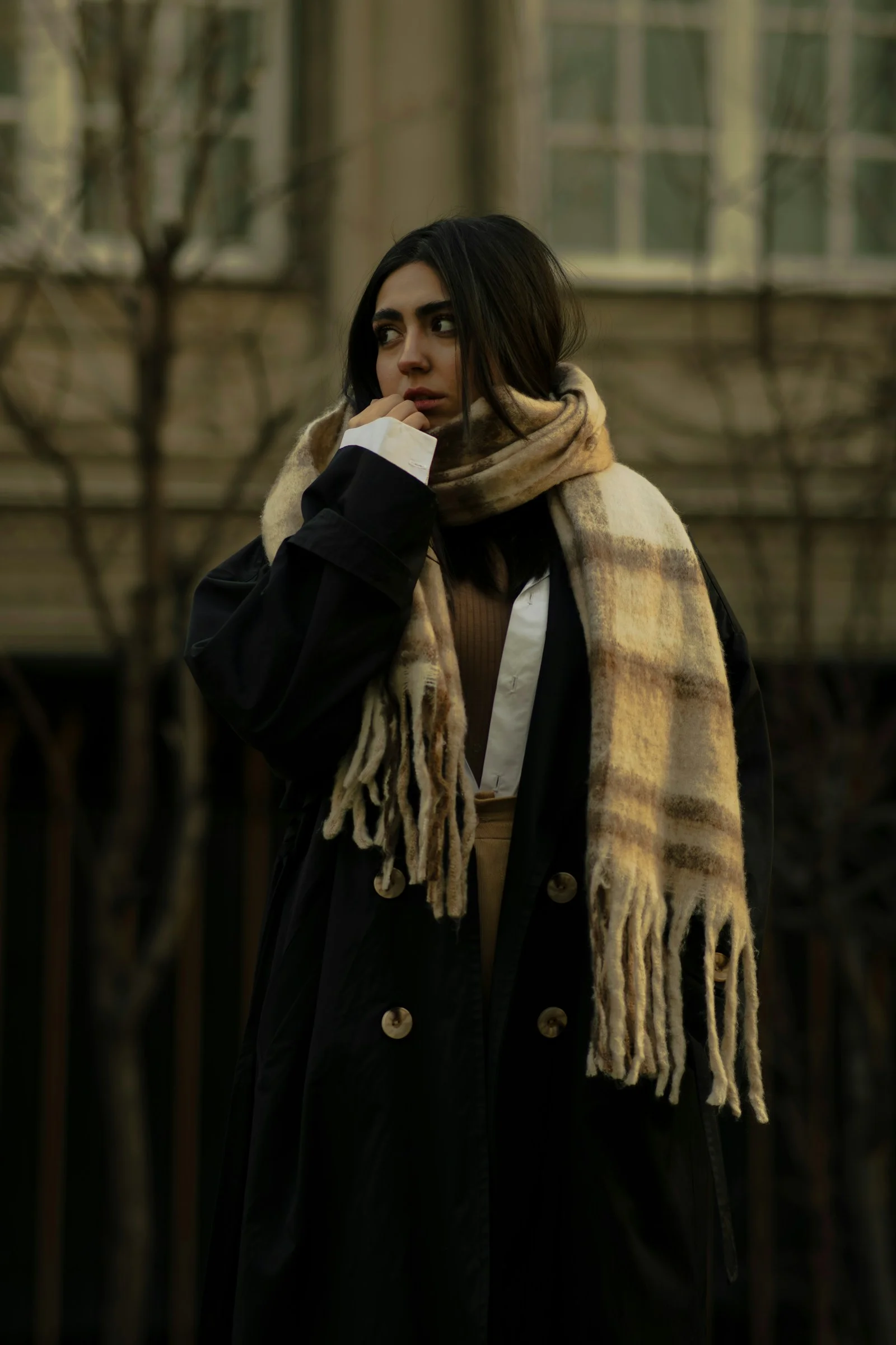 A woman wearing a black coat and a plaid scarf