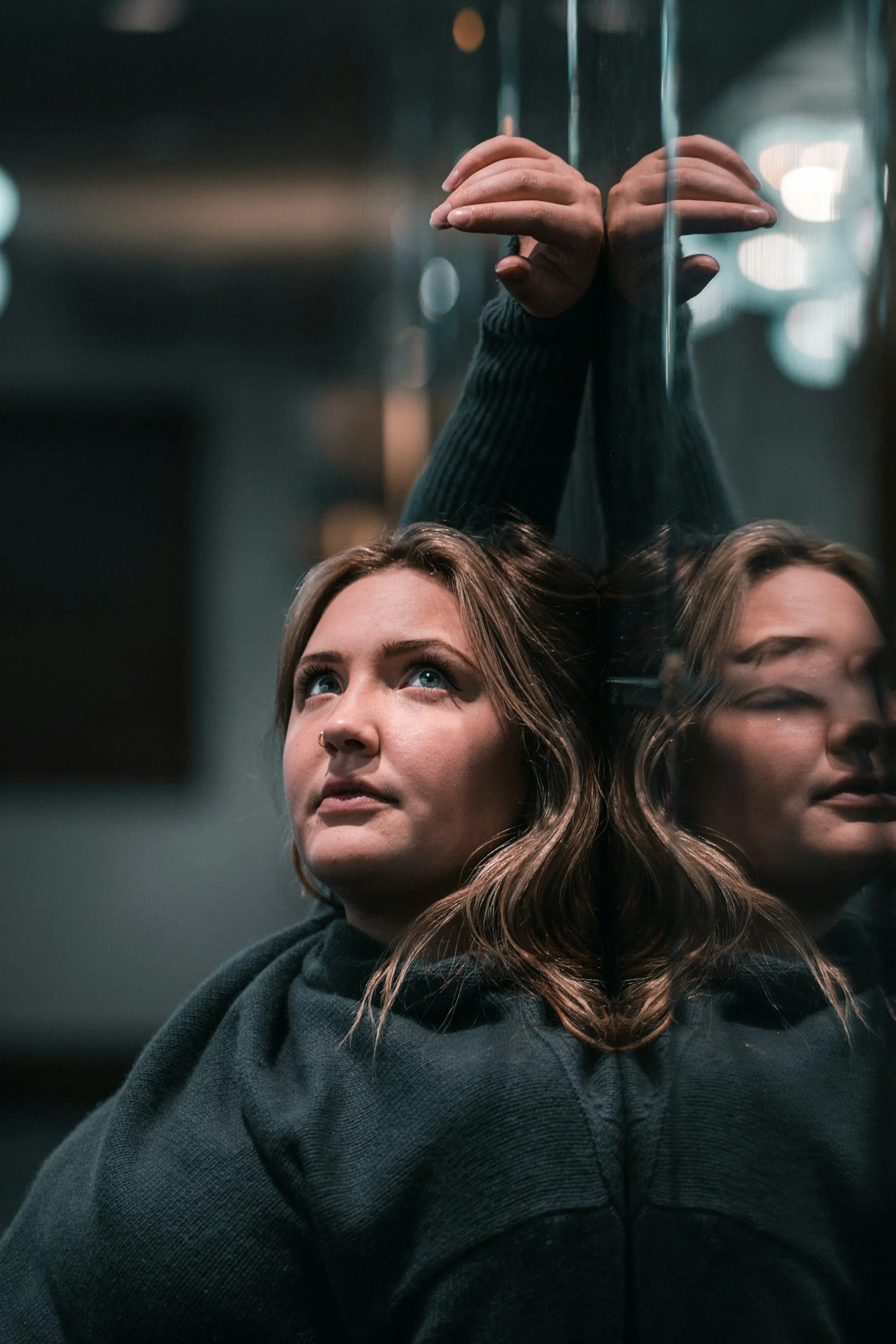 A woman in a dark sweater leaning against a reflective glass surface