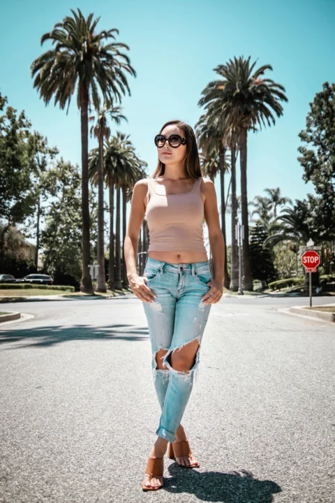 昼間、道路に立つ白いタンクトップと青いデニムショーツ姿の女性
