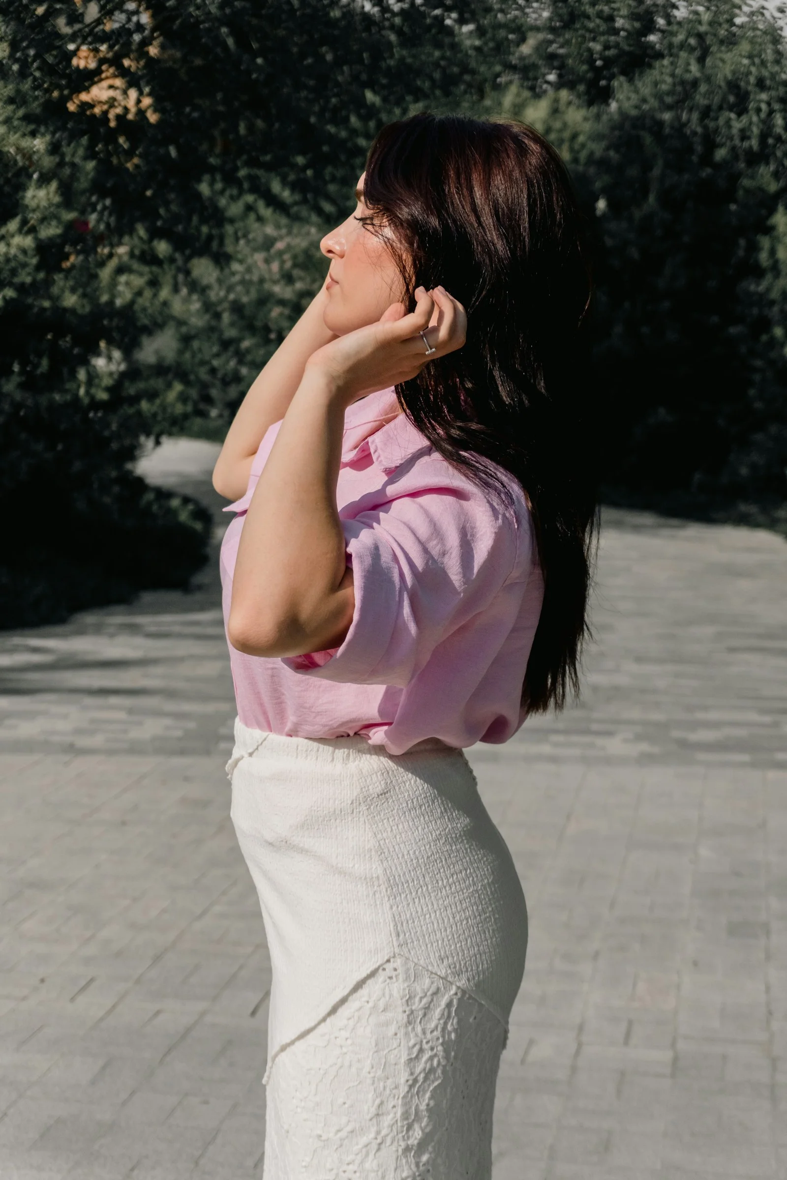 一名穿粉色衬衫和白色裙子的女人站在铺砌的小路上