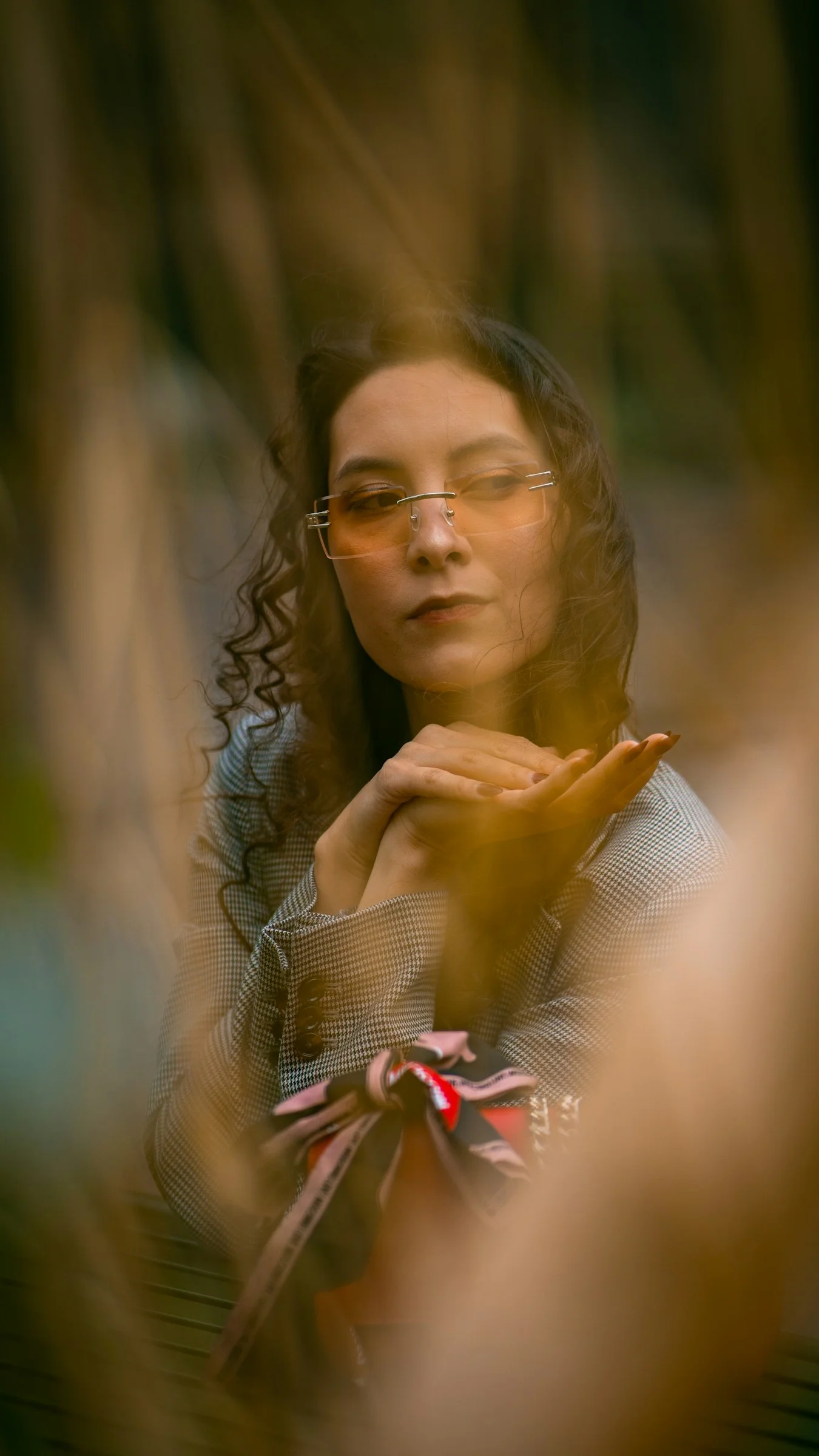 Woman with curly hair and orange glasses, hands clasped