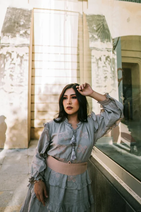 A woman poses gracefully near a weathered building