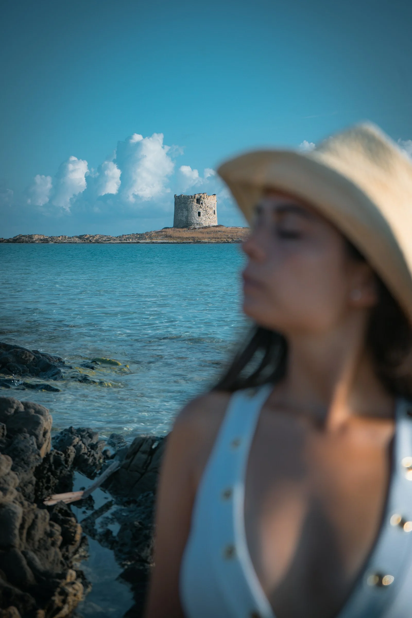 海辺の塔のそばにいる帽子をかぶった女性