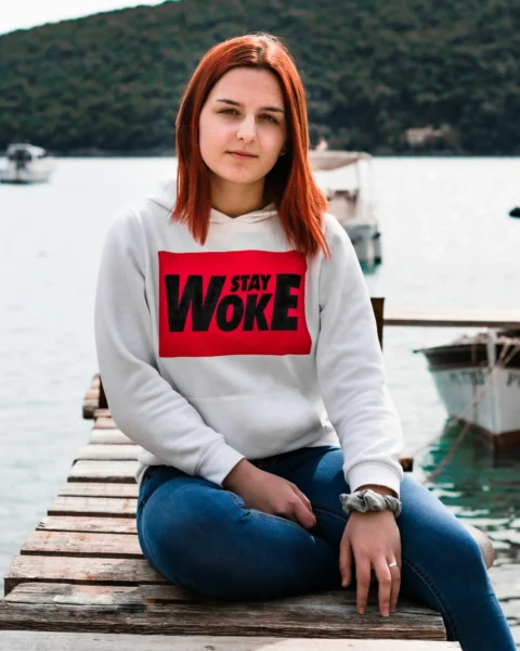 woman in white and red long sleeve shirt and blue denim jeans sitting on brown wooden
