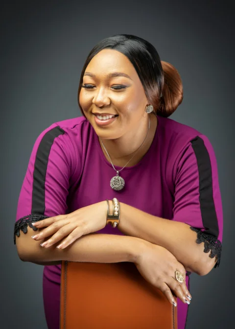 A woman in a purple top with black stripes leaning on a chair