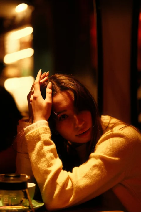薄暗い光の中で頭に両手を当てた若い女性