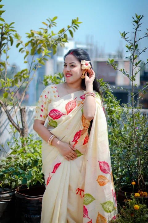 A woman poses in a saree, holding a flower