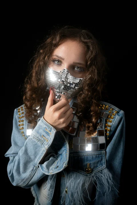 A woman wearing a disco ball mask and a denim jacket with studs