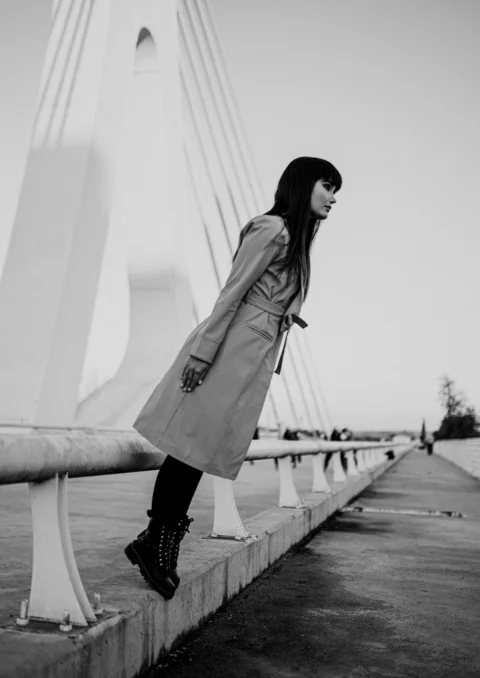 a woman in a trench coat leaning against a railing