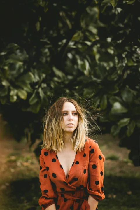 woman in orange coat standing near green tree during daytime